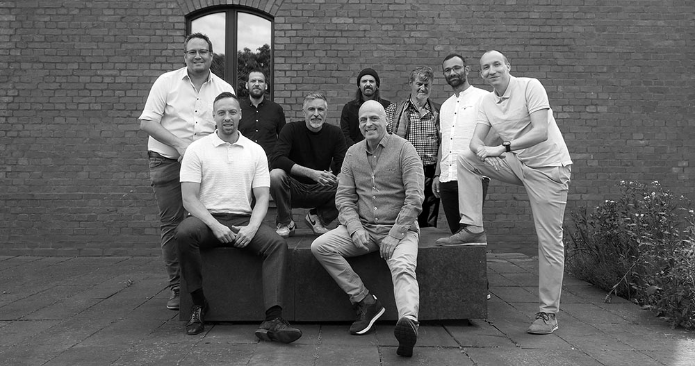 Team der IundS AG Berlin vor Backsteinmauer. Acht Personen in professioneller, aber lockerer Pose.